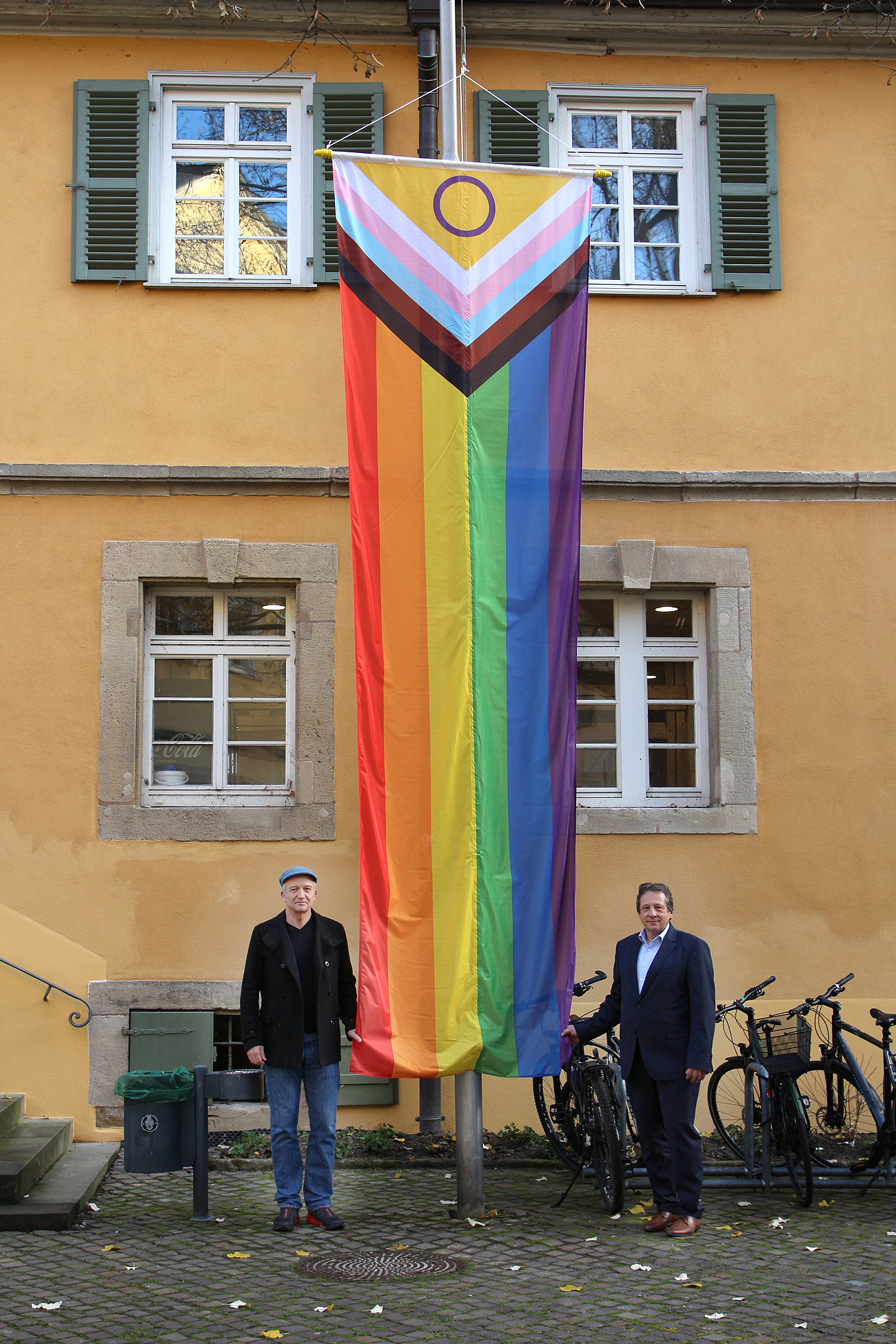 Prof. Pfister und Prof. Frey vor dem Hochschulgebäude mit gehisster Fahne der Toleranz