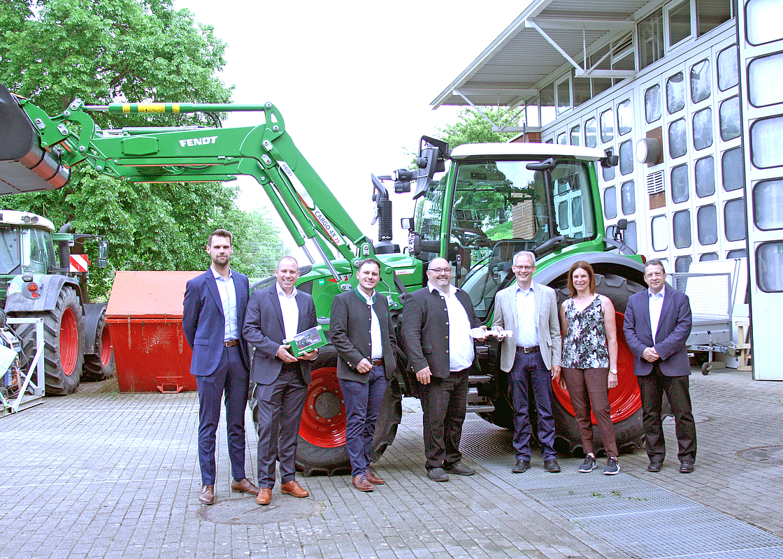 Sieben Personen stehen vor einem Traktor.  