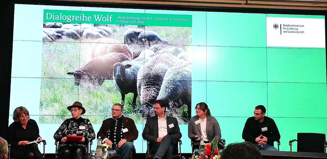 Prof. Markus Röhl mit sechs weiteren Teilnehmern auf der Bühne vor einem Bild mit Schafen