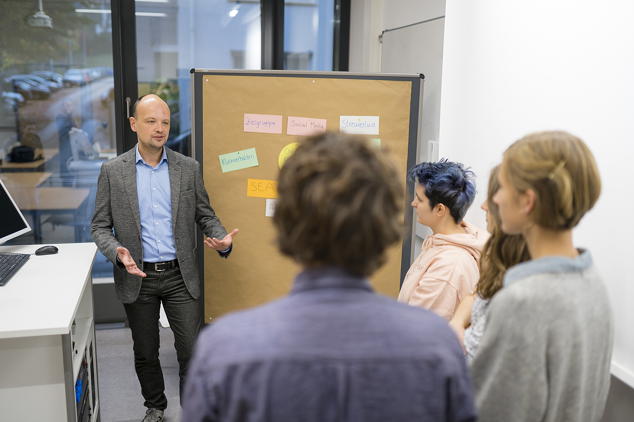 Dozent und Studierende besprechen eine Mindmap zum Thema Online-Marketing.