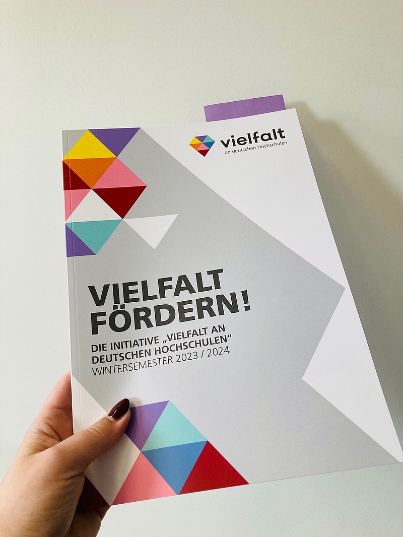 eine Hand hält eine DIN A4 Publikation mit dem Titel "Vielfalt fördern".